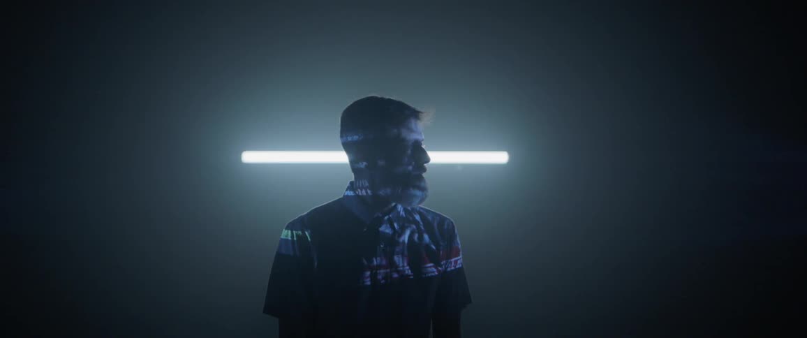 A bearded man in a darkened room has computerized text projected onto his face and head