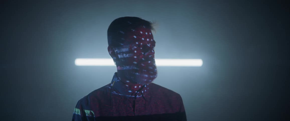 A man stands in a room with lighted designs projecting on his face and body