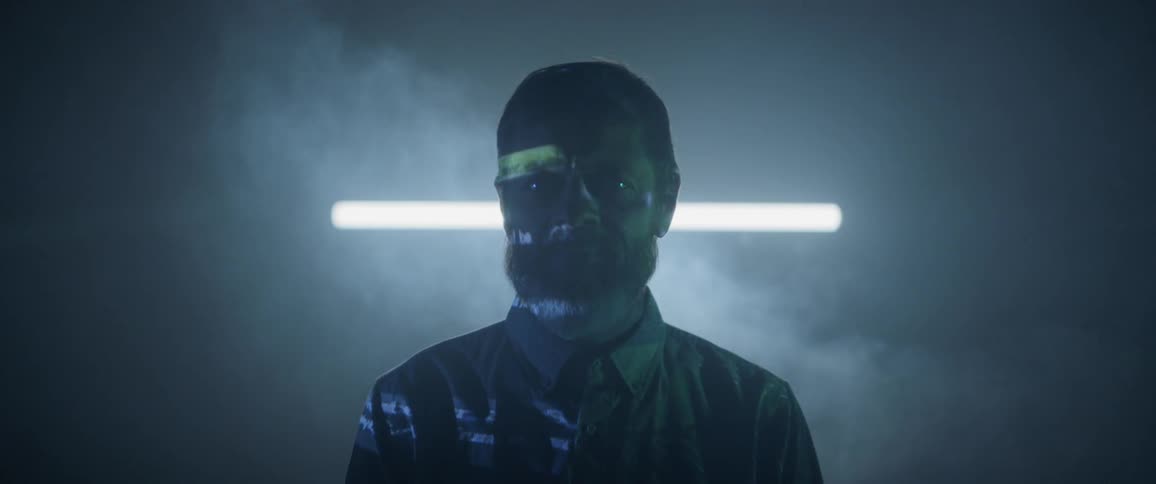 A man standing in a smoky and dark room while images being projected on his body