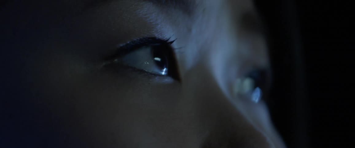An asian woman looks up and to the side as words and lights are projected on her face