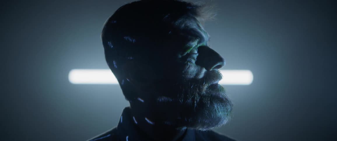 A man stares to the side while lights and patterns wash over his face