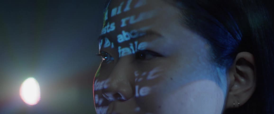 A young asian teenager stares ahead as lights flash across her face