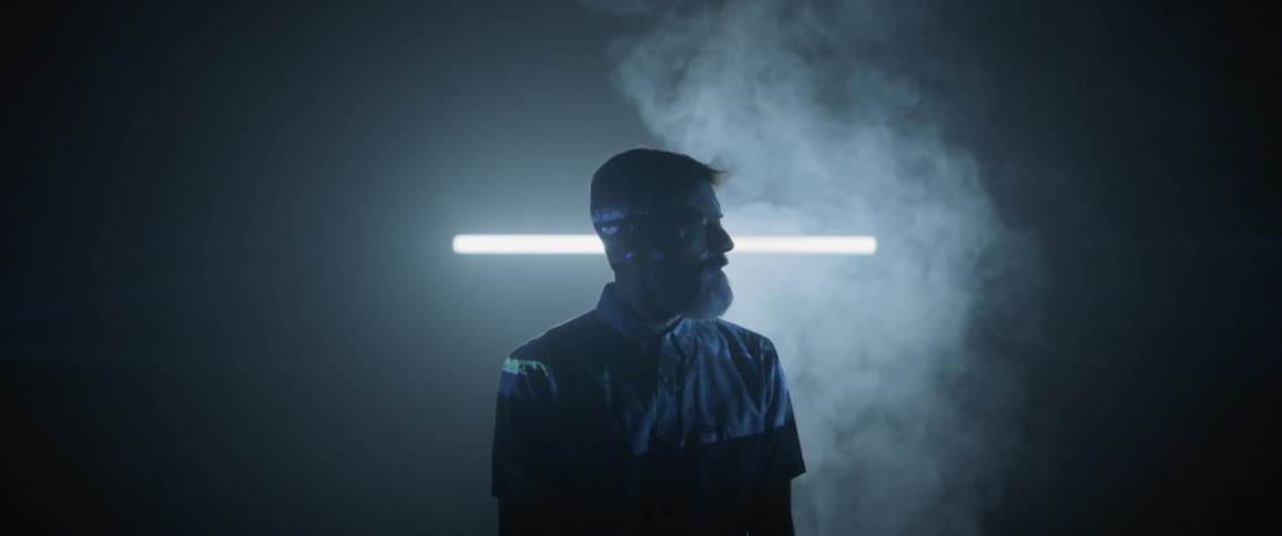 Man standing in smoke in dark room with projection lights on him