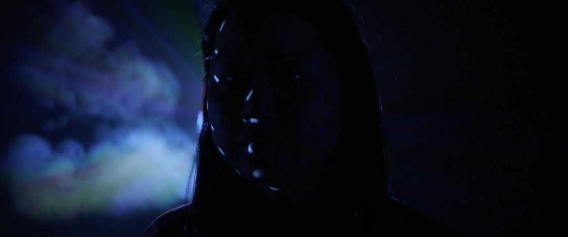 An asian girls sits while lights flash on her face