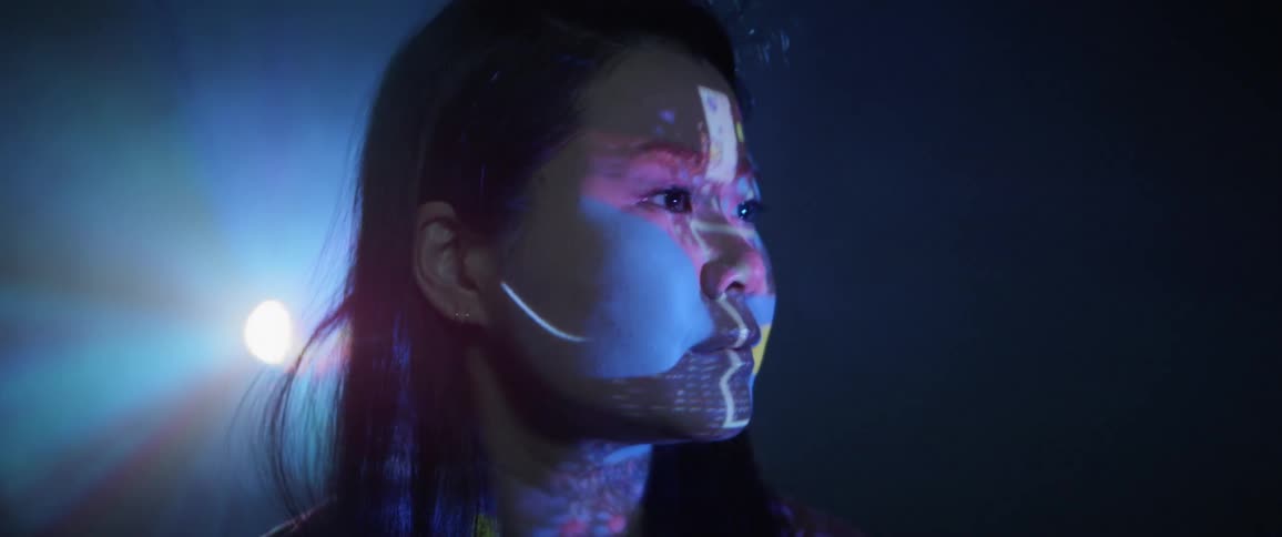 An asian girl looks atscreen as lights cross it and reflect on her face