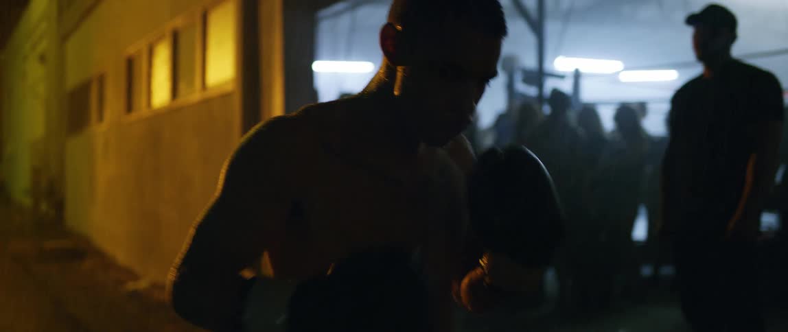 A man hitting himself in the face with boxing gloves outside a crowded building in the rain