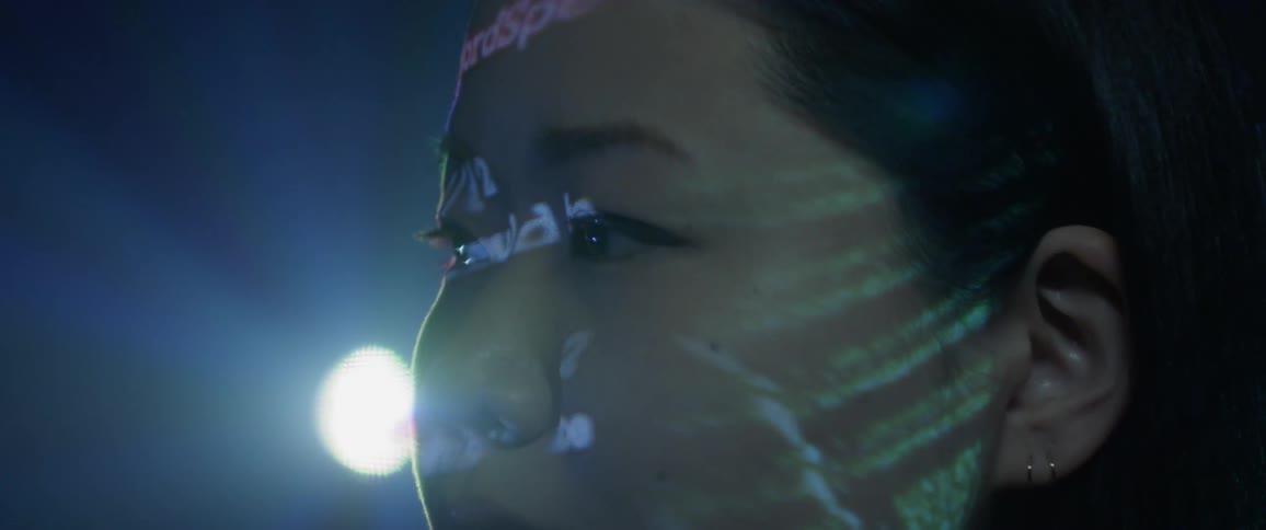 A woman standing in a dark room with art projected onto her skin