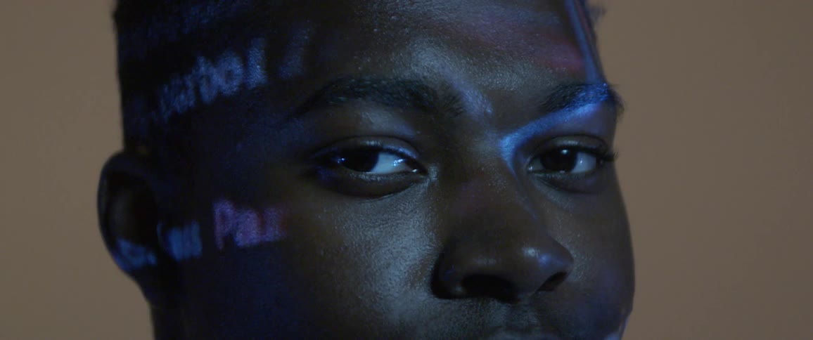 A black male teenager blinks as lights and text flash across his face