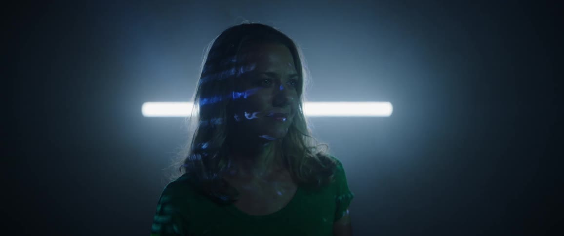 A female stands inside of a darkened room while computerized text is projected onto her face