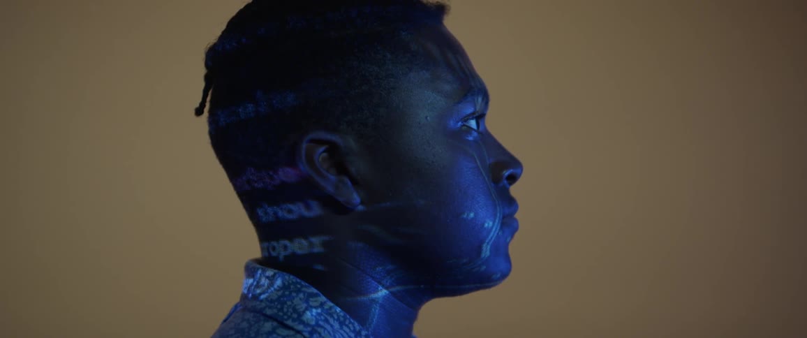 A young black man looks at a screen as the lights reflect on him
