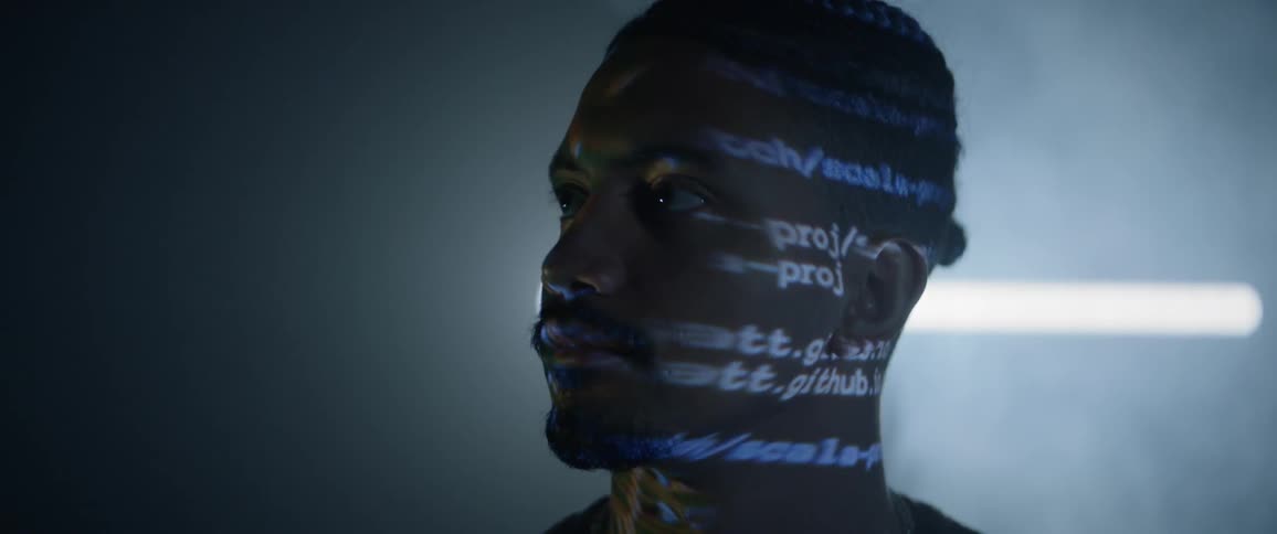 A black man looks ahead as lights reflect on him