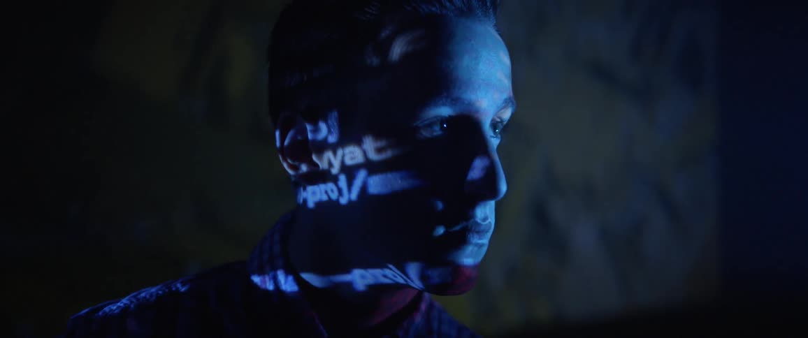 A young man looks ahead as bright lights flash and text is projected on his face