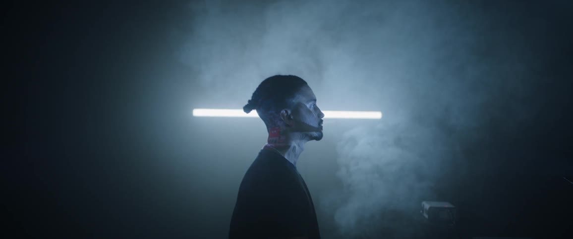 A black man stands in a smoky room as lights flash