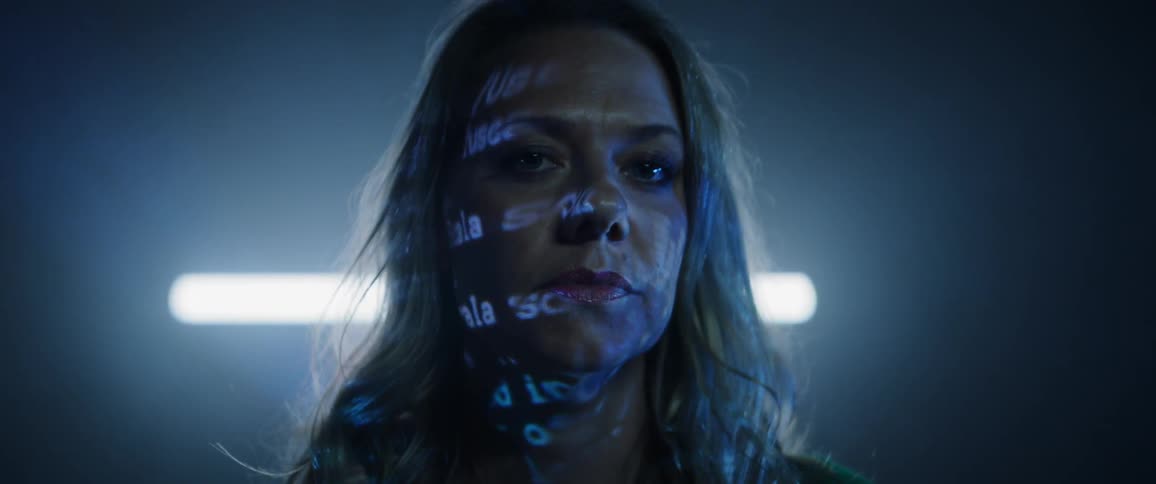A women turns her head to look straight ahead while words and lights are projected on her face