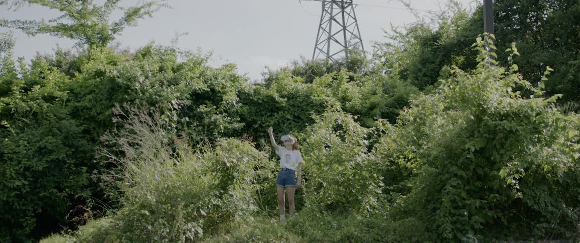 A woman outside in the bushes with virtual reality goggles on