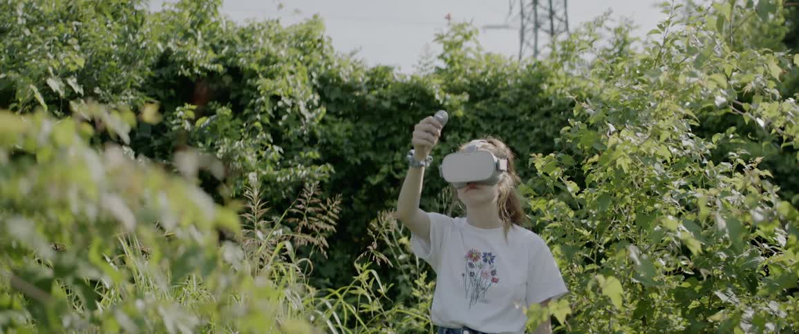 A girl in a yard wearing a vr headset lifts her arm moving a controller