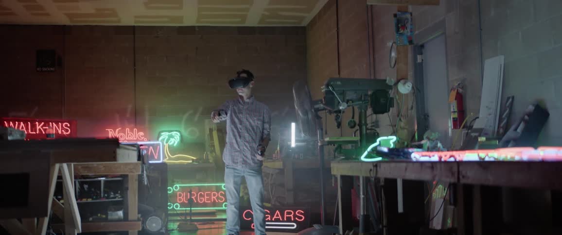 A man with virtual reality goggles in a room with neon light signs in the back