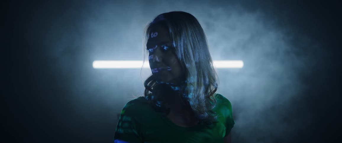 A woman standing in a dark and smoky room as text is projected onto her body