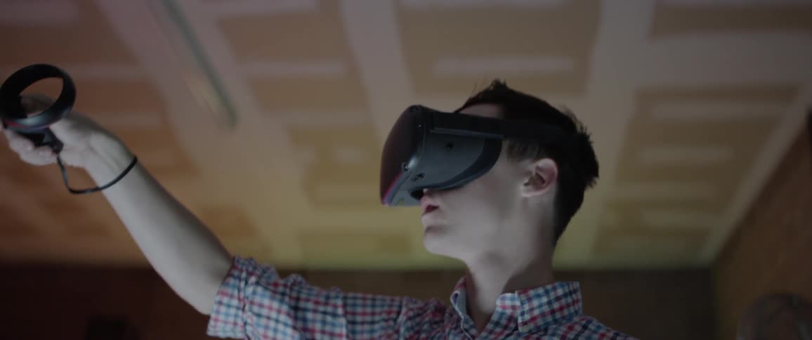 A young man with virtual reality goggles on moves his arm in the air