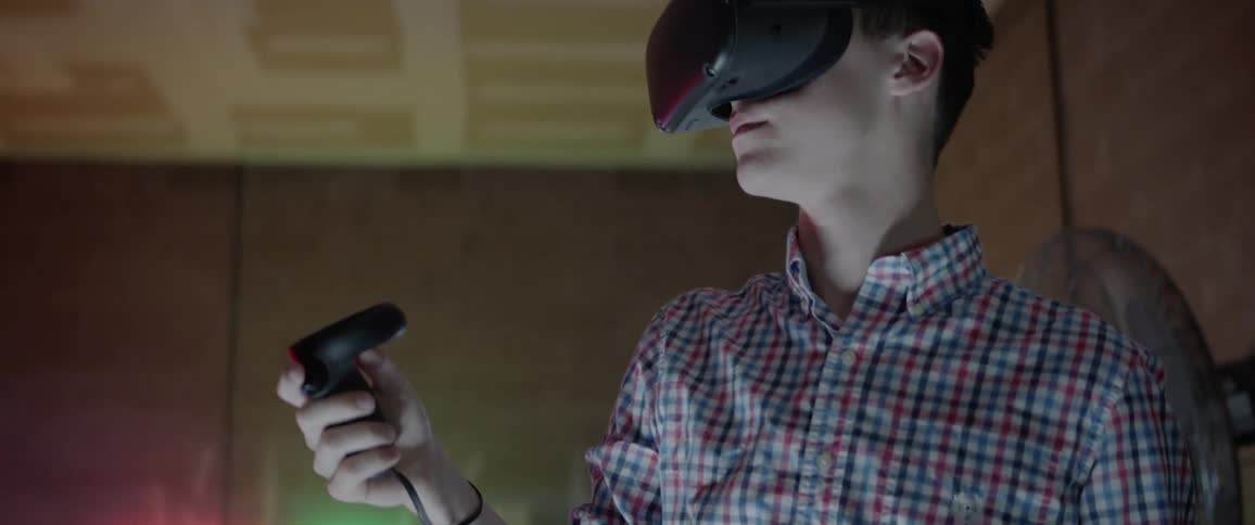 A young male holds a controller above his head while wearing a virtual reality headset