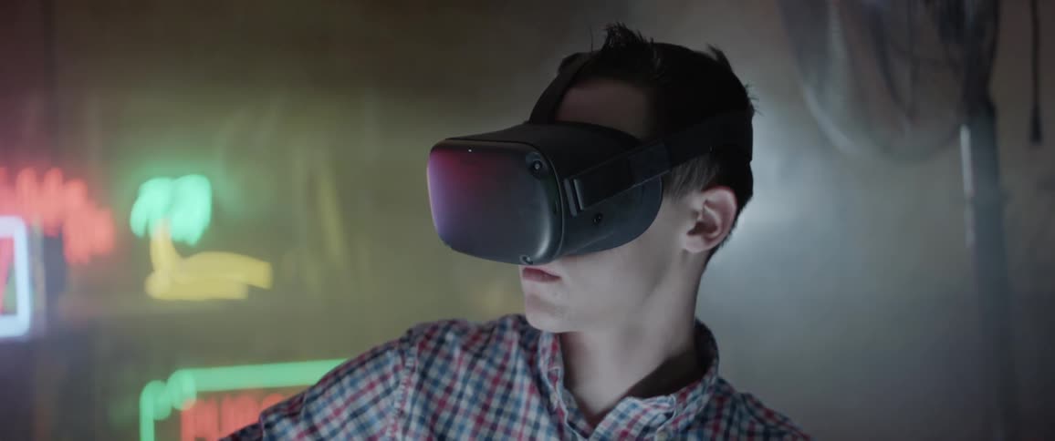 Man plays game wearing vr goggles in dim room decorated with neon signs