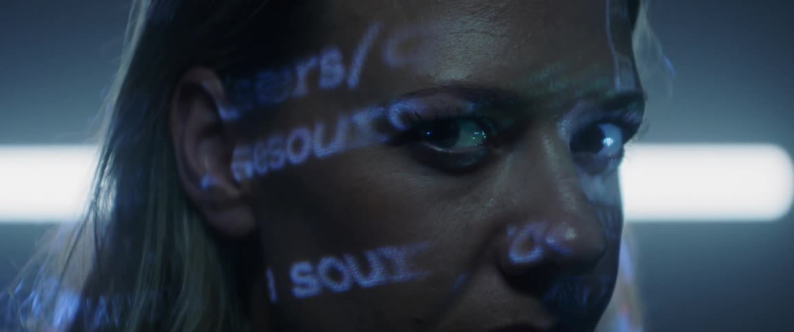 A woman gazing into the camera as code is projected on her face