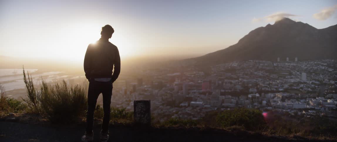 A young man stands on a hill and looks down at the city