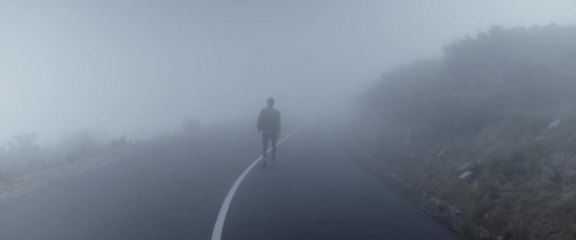 Man walks along the asphalt road through the fog