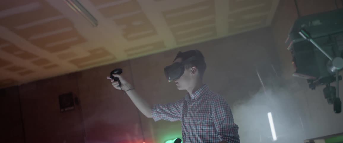 A young man with virtual reality glasses on stands and moves his arms and looks around