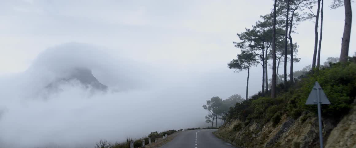 Heavy clouds and fog cover a mountain peak and a hilltop road