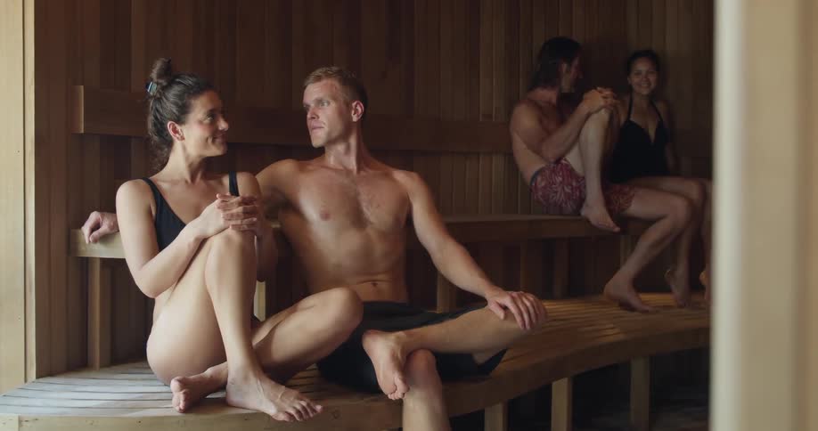 Two couples in bathing suits sit on wooden benches in a sauna