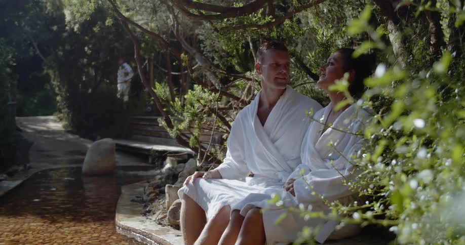 A man and a woman sit on a stone bed paddling their feet and talking