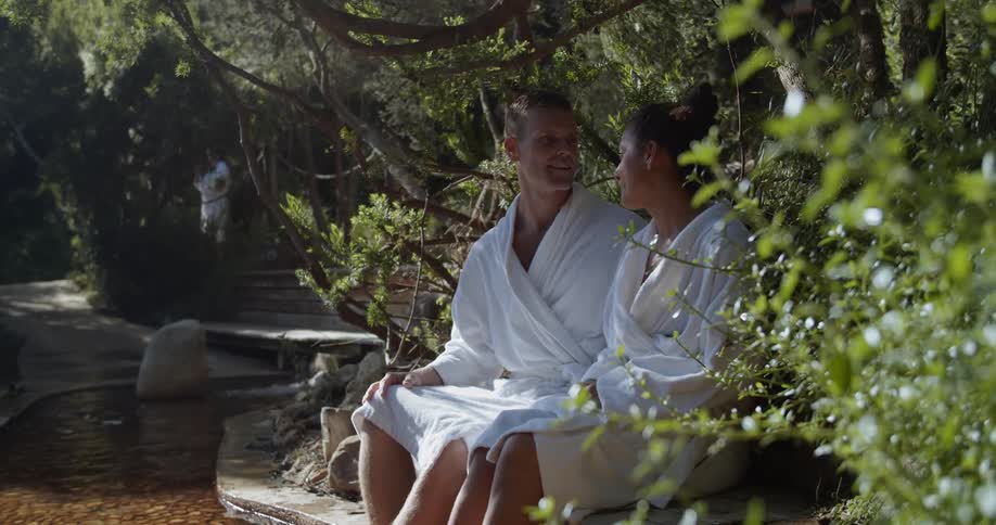 Man and woman sit on bench soaking feet in stream