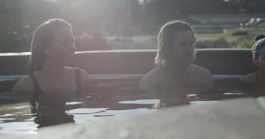 People relaxing in a kind of thermal bath surrounded by bushes as the sun reflects off of the water