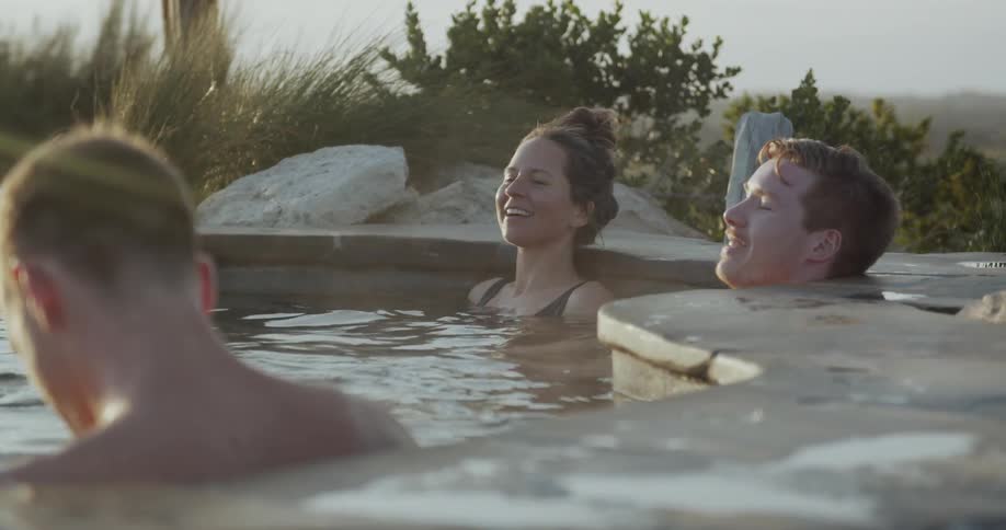 Steam rises from the heated outdoor spa as people laugh and relax while soaking