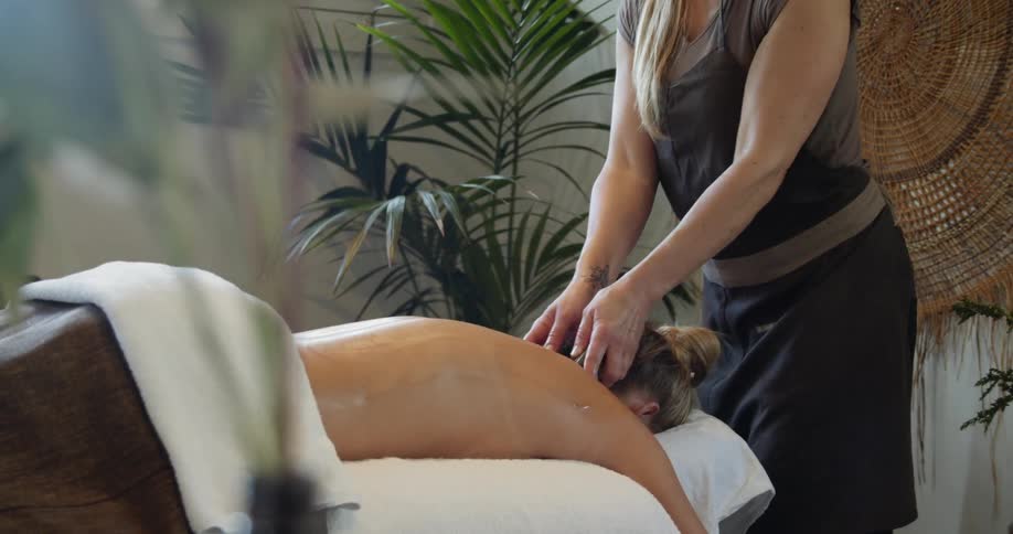 Female masseur massages for blonde womans back at spa center