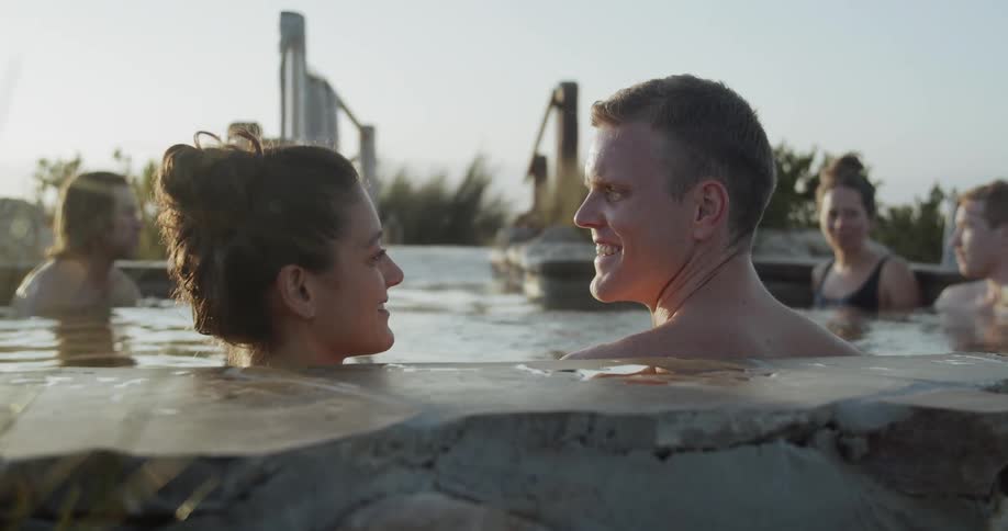 A group of people relaxing in a kind of thermal bath surrounded by bushes