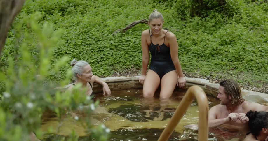 A group of people relaxing in a kind of thermal bath surrounded by bushes