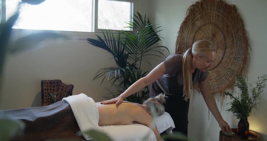 A masseuse applies oil to a clients back and rubs it in