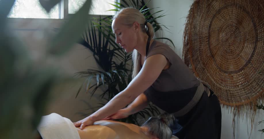 Female masseur massages for blonde womans back at spa center