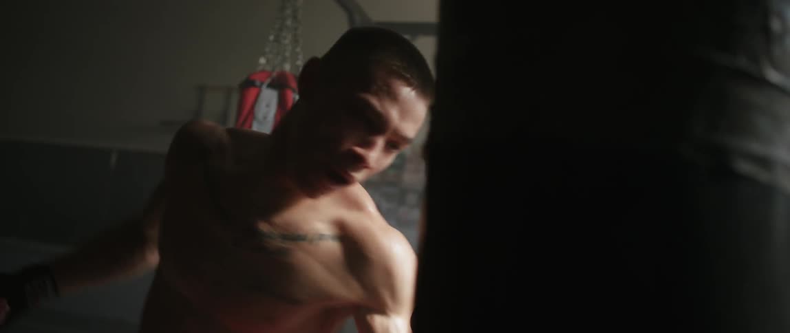 A shirtless man wearing boxing gloves and hitting a punching bag