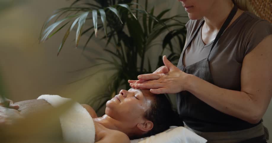 A woman lies on a massage table as another woman rubs her face