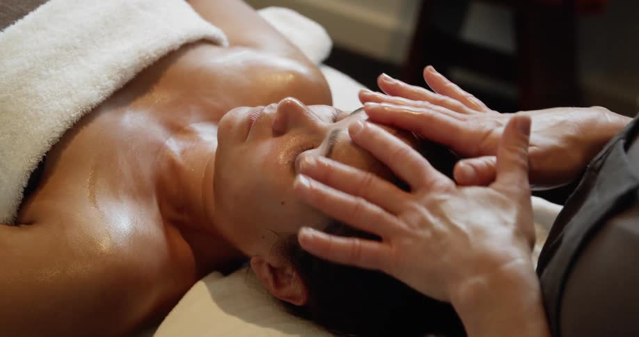 A woman gets a facial massage while laying on a table