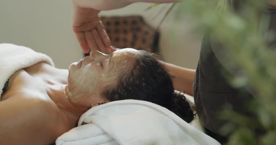 A woman lies on a table as another woman gives her a facial
