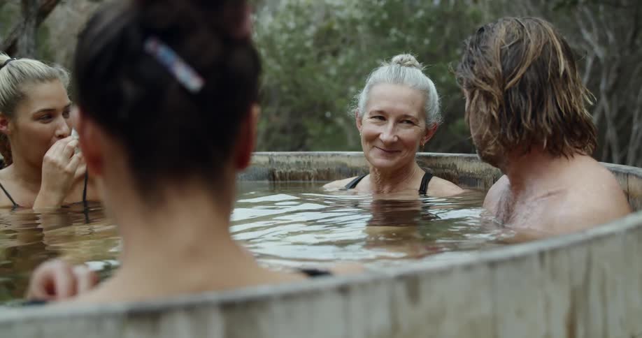 A group of people relaxing in a kind of thermal bath surrounded by trees