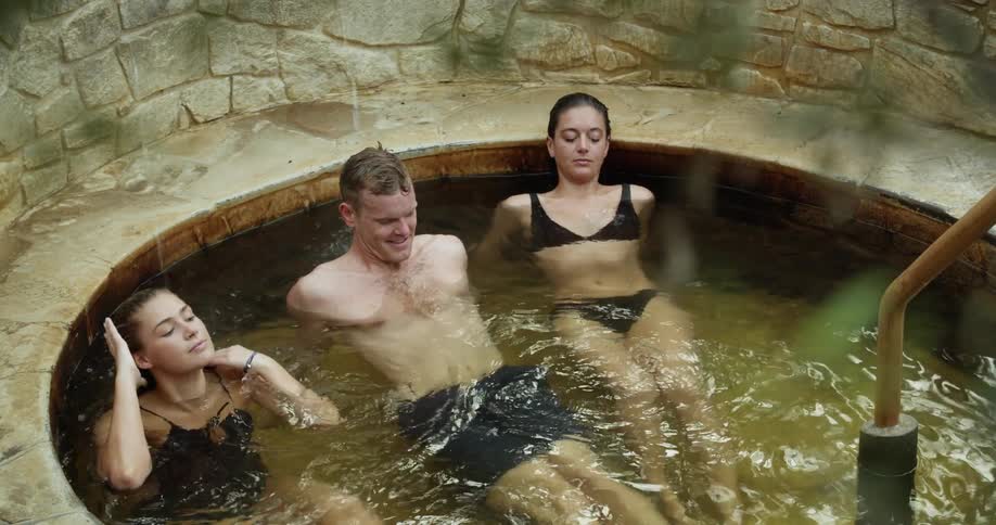 Two women and a man relax in a stone clad thermal bath