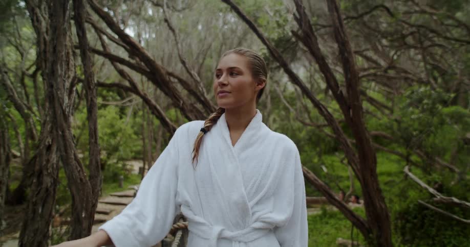 A woman wearing a bathrobe walks along an outdoor path through a wooded area