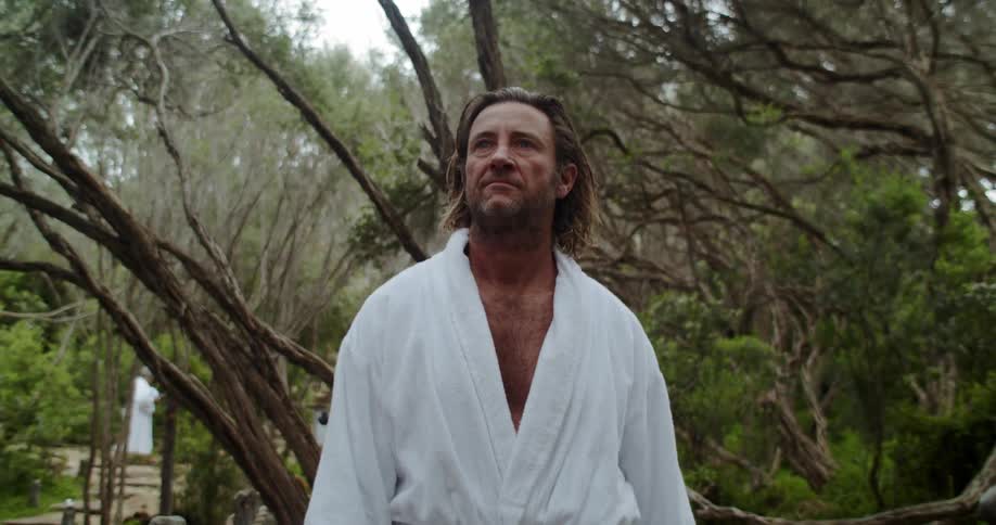 Man wearing robe walks along path outdoors among trees