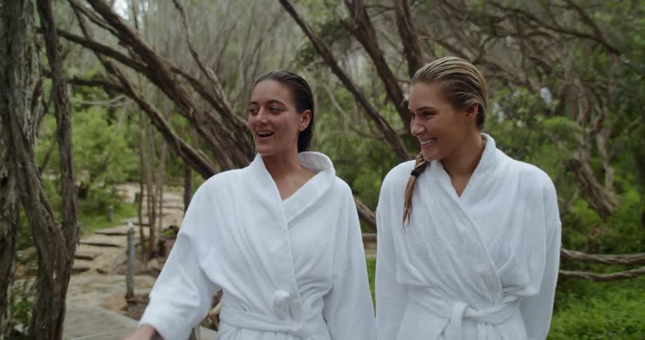 A pair of women in white bath rooms walking along a path through an arboretum