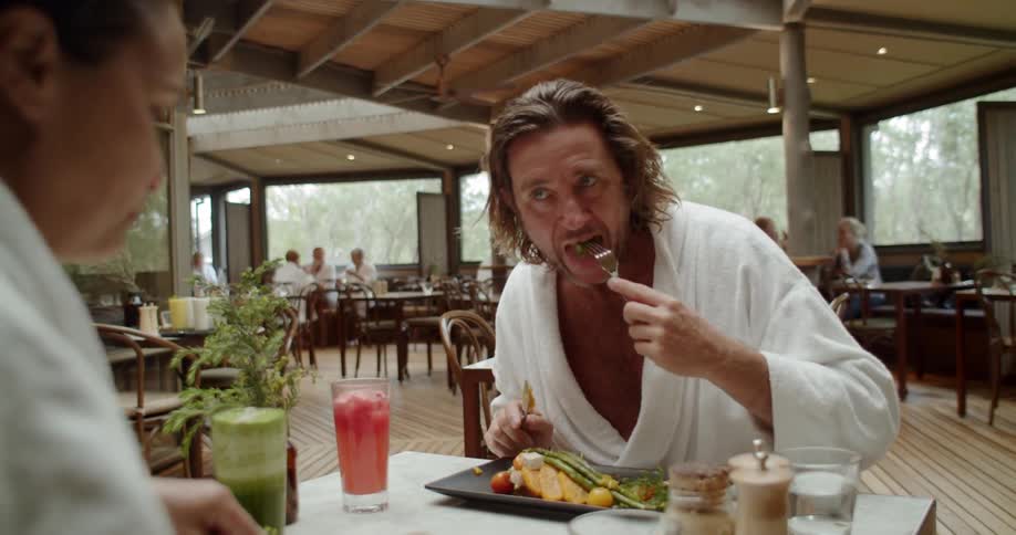 A man and woman in white bath robes eating in a restaurant